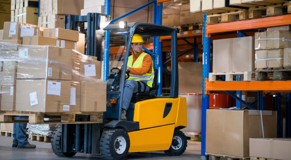 Man in warehouse operating a lift machine to transport boxes