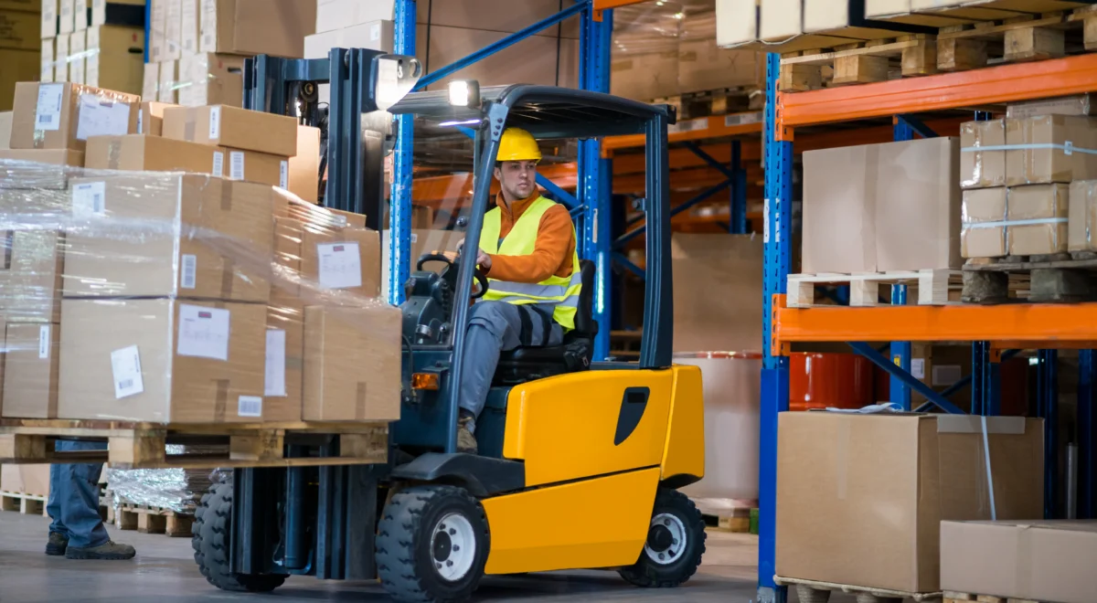 Man in warehouse operating a lift machine to transport boxes