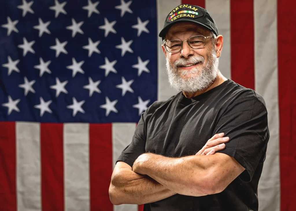 Vietnam War Veteran standing with arms crossed while smiling in front of American flag background